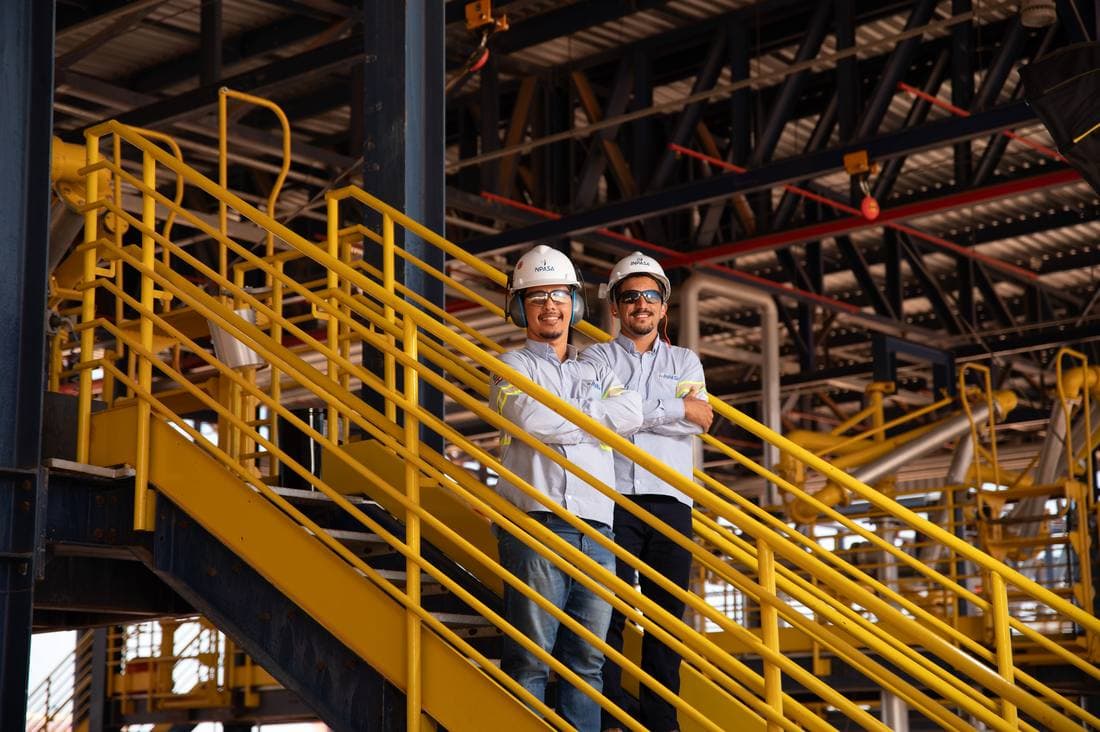 Dois funcionários de capacete e uniforme Inpasa sorrindo na escada de uma unidade industrial